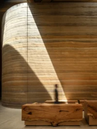 Curved rammed earth wall lit by a shaft of daylight above a carved timber console