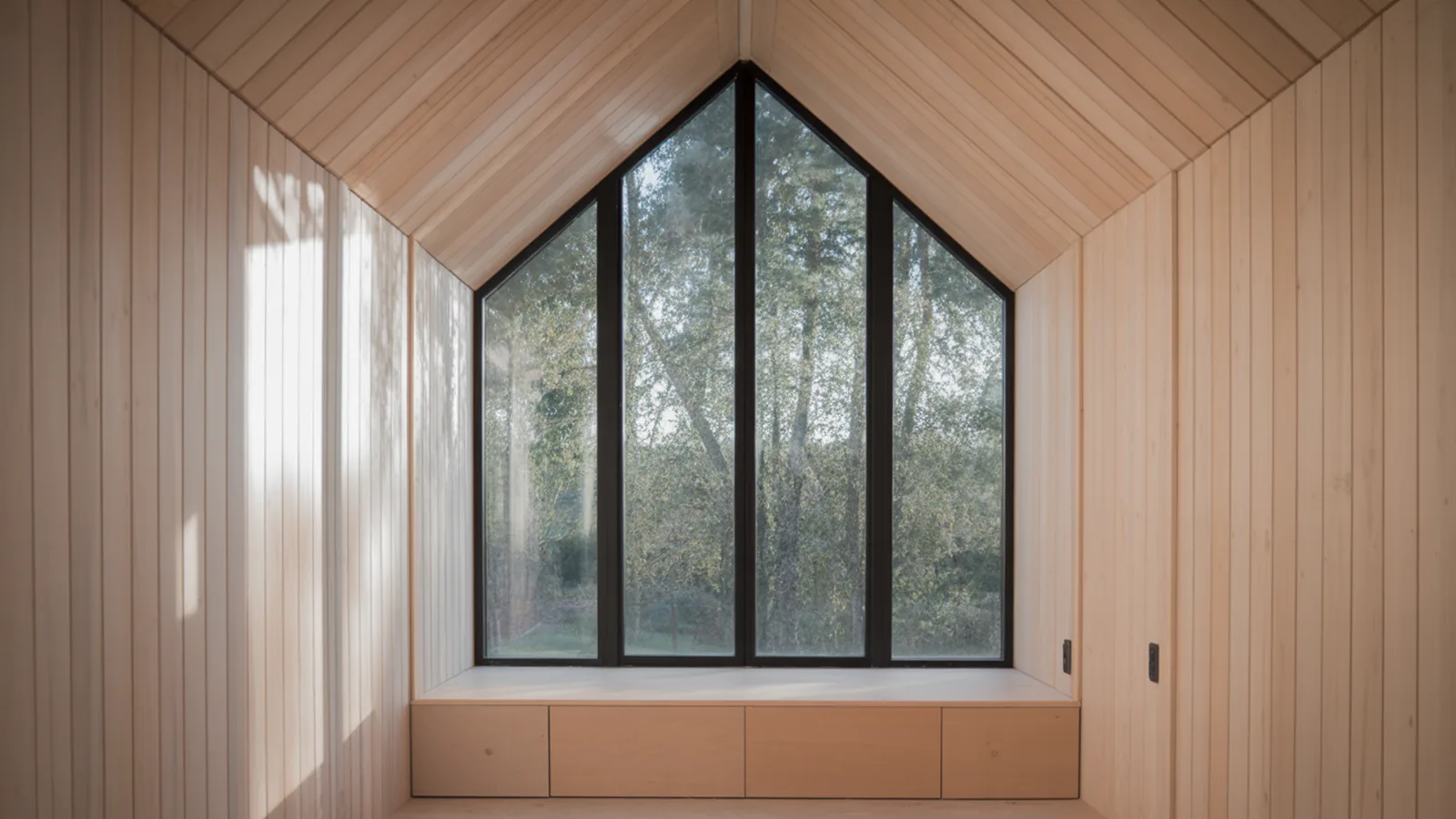 Tiny house interior with full height gable glazing opening to trees and a built-in bench below