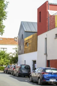 Street view of the white house with its zinc gable and the timber guardrail wrapping the roof, Inhabiting the Roof by Paris Atlas