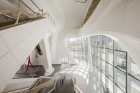 Multi level void with white sculptural columns, stairs and the diamond gridded glass wall inside KAFD Metro Station by Zaha Hadid Architects
