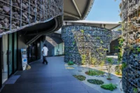 A visitor passing the gabion wall at Future Life Village Pavilion by KOMPAS