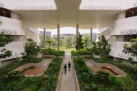Shaded courtyard under a wavy white canopy with raised planters and timber seating, Singapore Institute of Technology by Henning Larsen