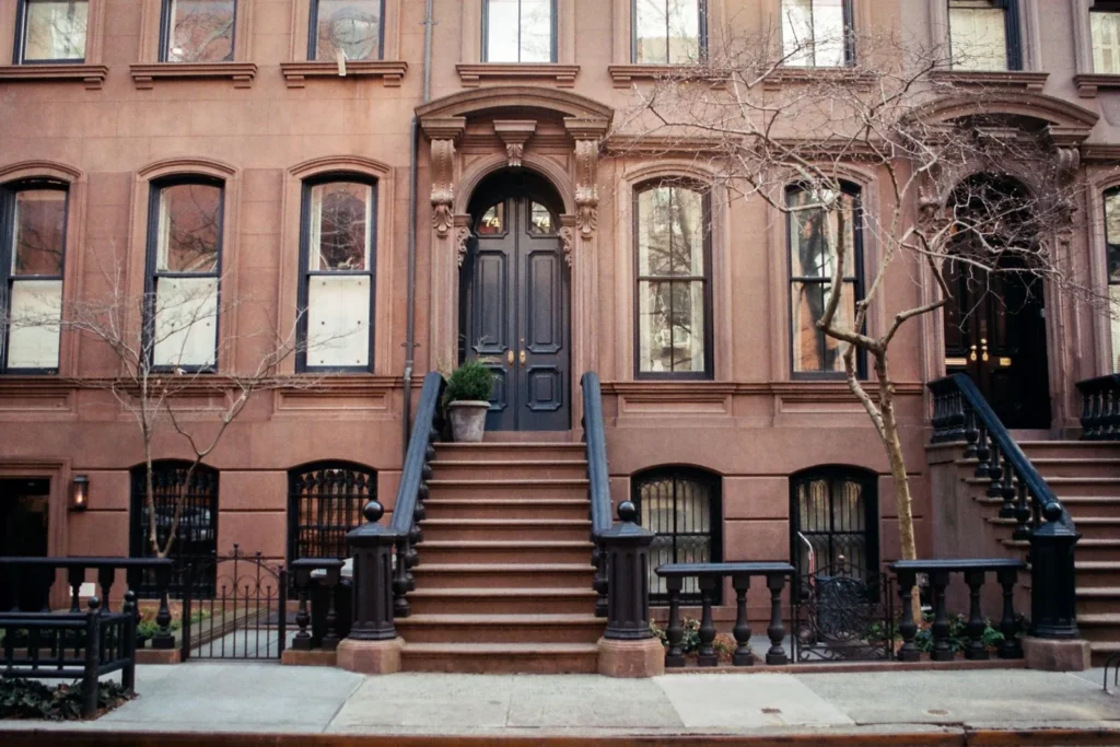 Brownstone row house with a high stoop and arched entrance on a tree lined street