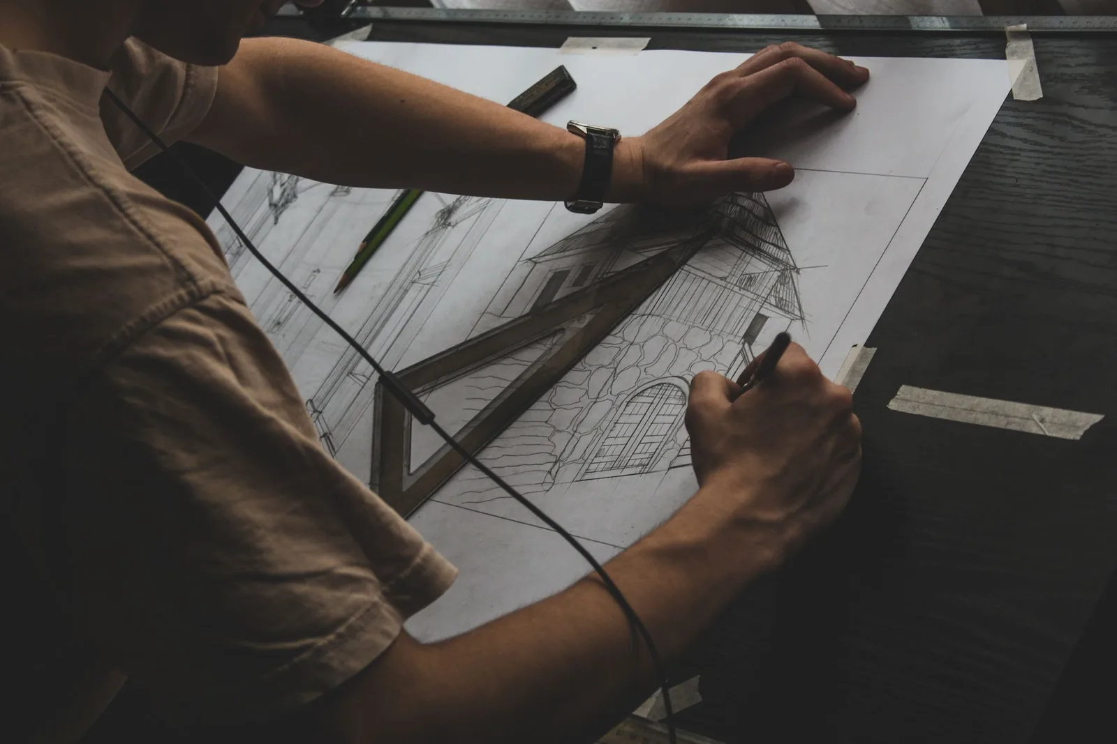 Architecture student sketching a house perspective in pencil on a drafting table with a set square
