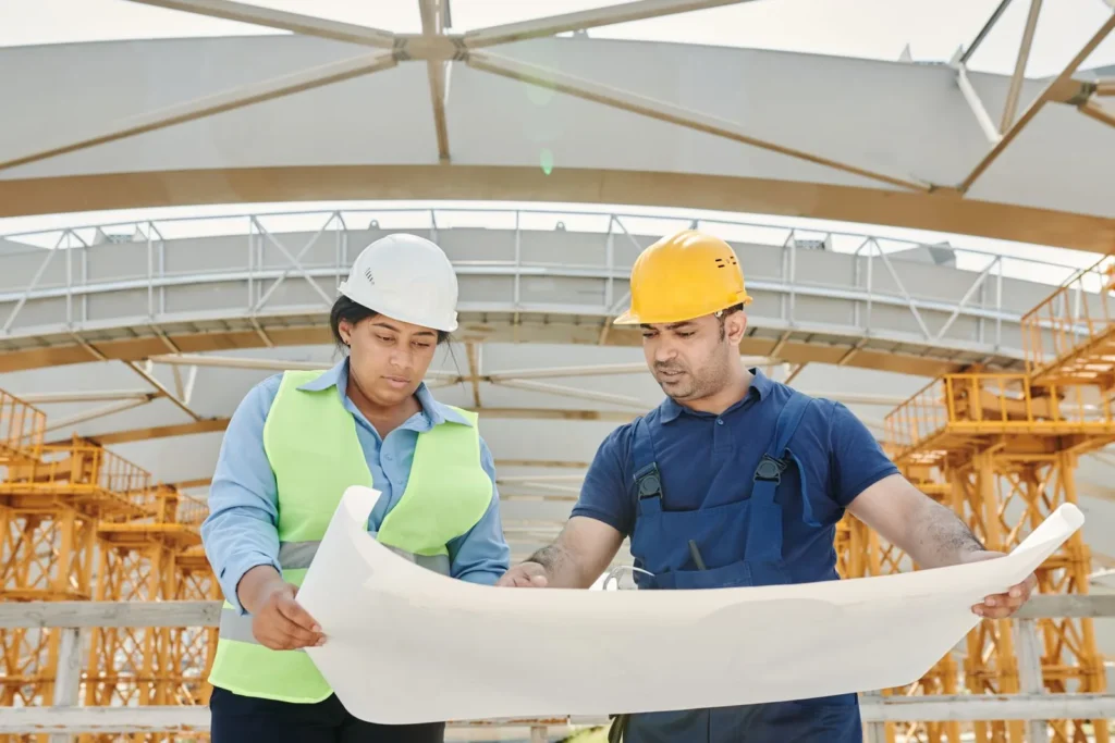 Two engineers in hard hats reviewing a large drawing together on a construction site