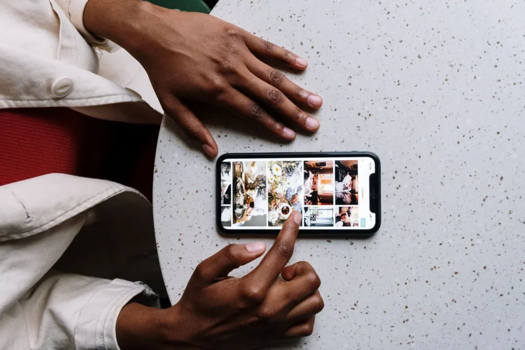 Hands browsing a grid of saved images on a phone lying on a speckled table