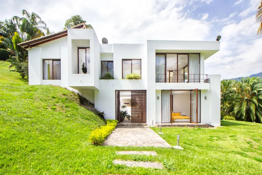 White modernist house stepping down a grassy hillside with large openings to the garden
