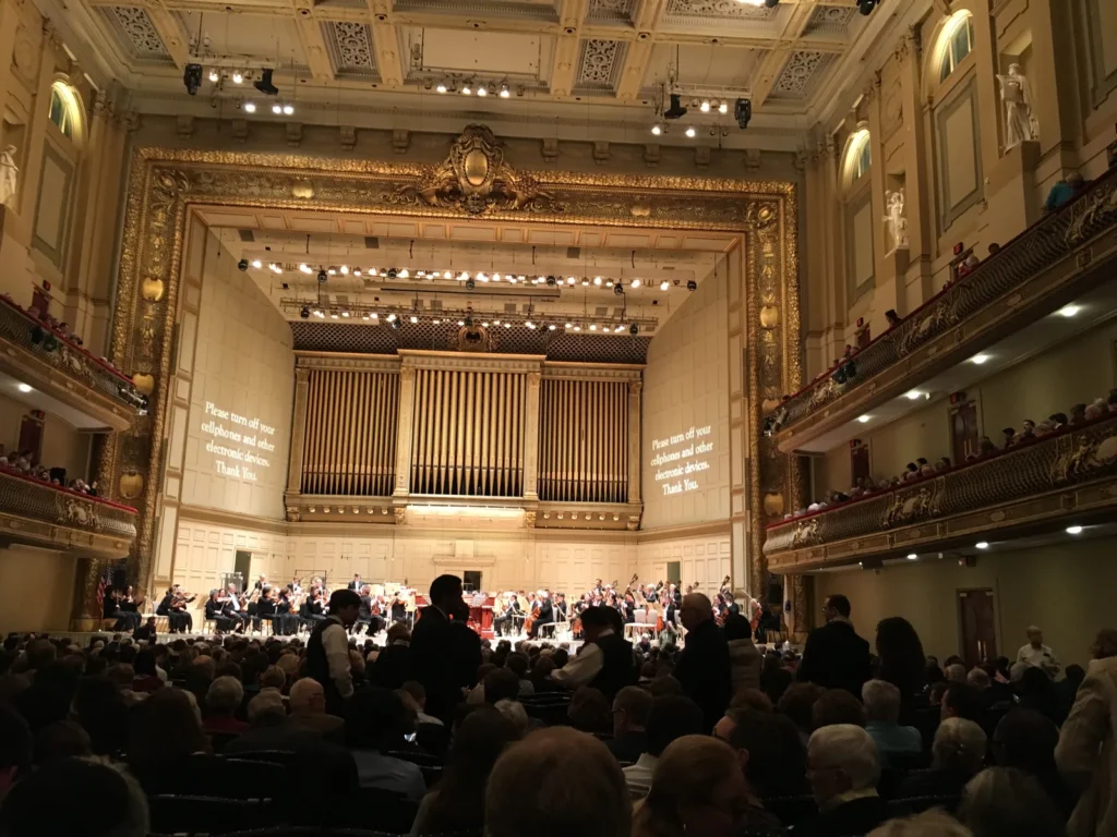 Audience filling the shoebox hall of Boston Symphony Hall before a concert, with the organ and statue niches behind, a benchmark in concert venue architecture