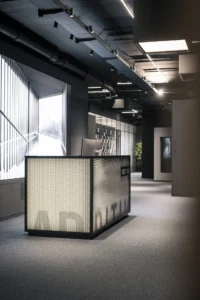 Reception counter of backlit perforated metal with a partly hidden logo near the entrance, ADDITIVE HQ by NOA