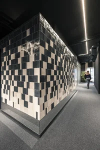 Corner of a box clad in a pixel pattern of blue and cream tiles with a light strip above, ADDITIVE HQ by NOA