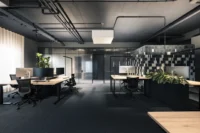 Workspace with height adjustable desks and task lamps beside a tiled box and planters, ADDITIVE HQ by NOA