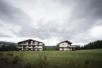 The two freestanding hotel buildings standing apart in an open meadow under a cloudy sky, Aeon by noa*