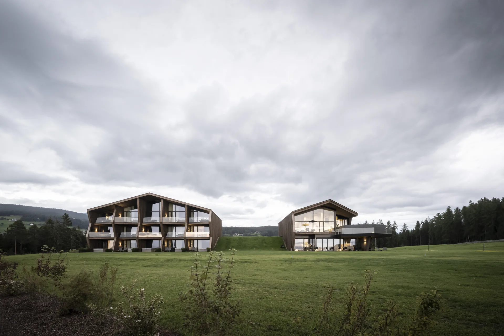 The two freestanding hotel buildings standing apart in an open meadow under a cloudy sky, Aeon by noa*