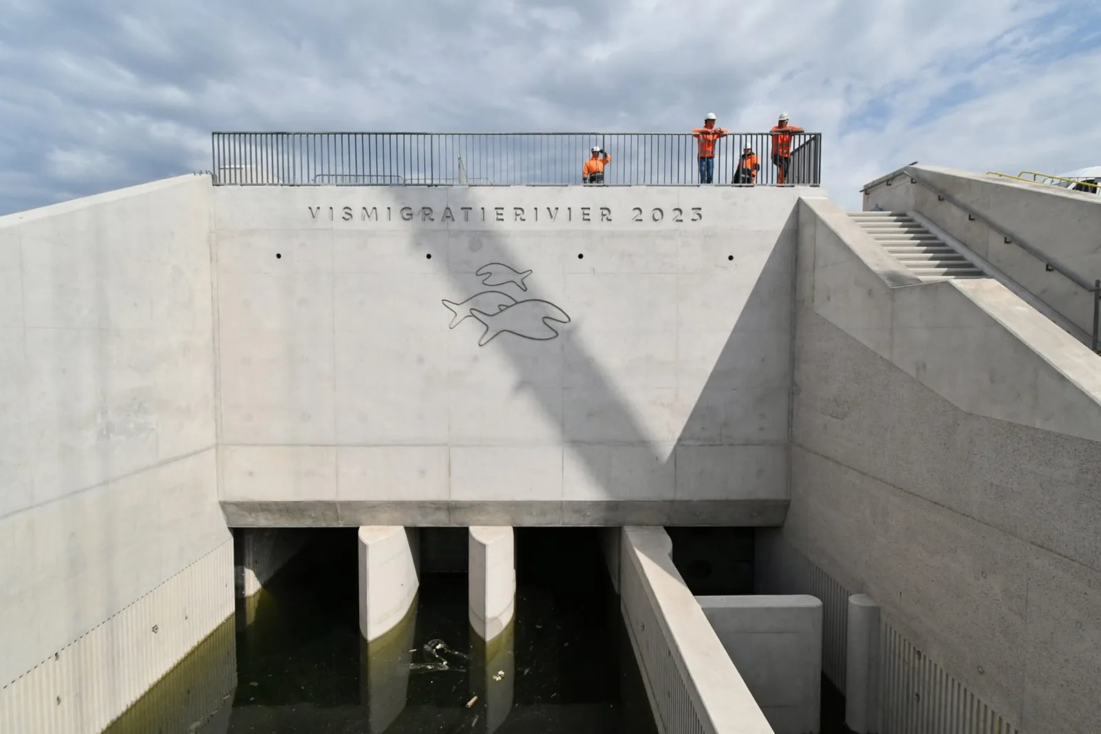 Concrete fish passage structure with an engraved fish motif and people standing on top