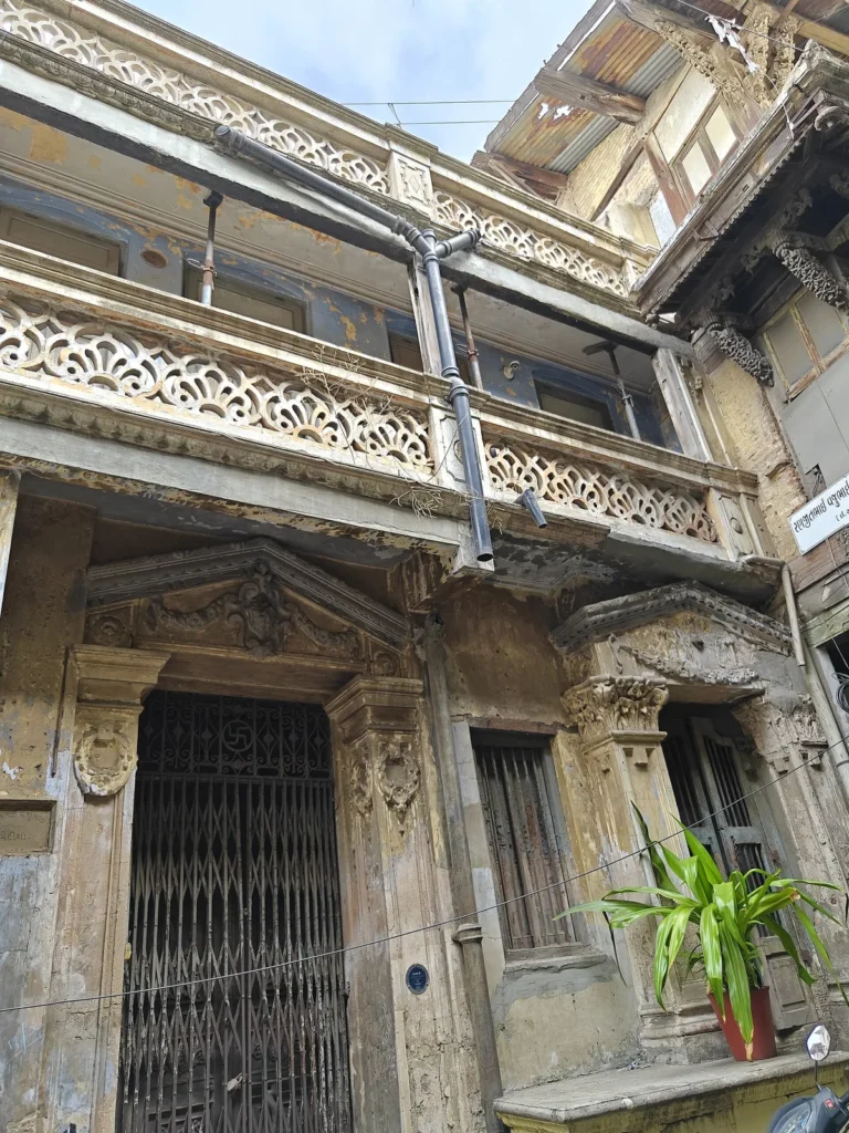 Weathered colonial style pol house with carved balconies and an iron grille door in old Ahmedabad