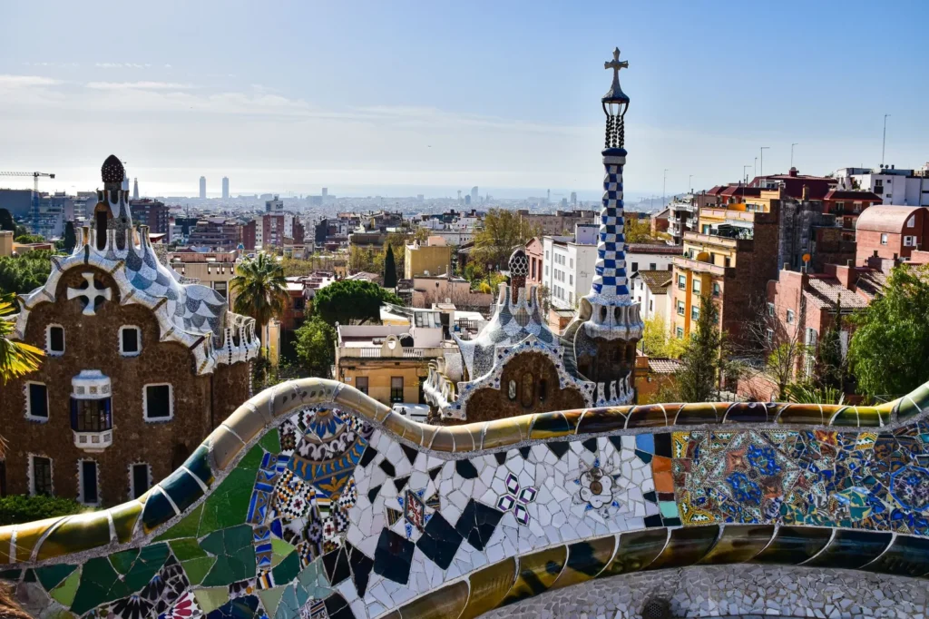 Antoni Gaudi architecture at Park Güell, with the serpentine trencadís bench and gatehouse towers overlooking Barcelona