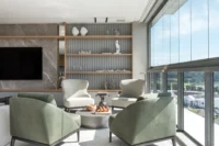 Lounge with sage green armchairs before grey stone and shelving, Apartment Elache by Caroline Andrusko Arquitetos