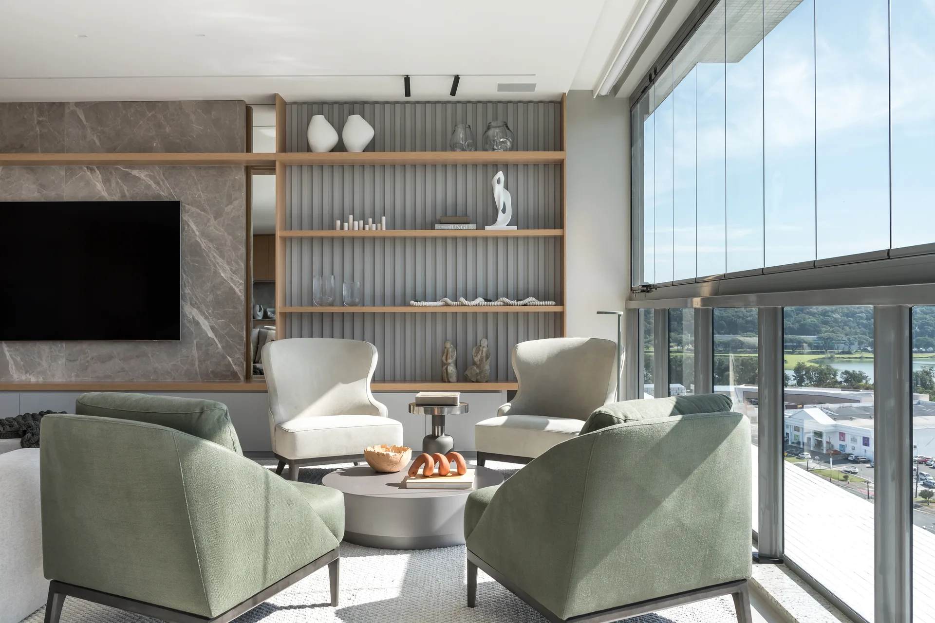 Lounge with sage green armchairs before grey stone and shelving, Apartment Elache by Caroline Andrusko Arquitetos