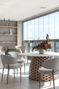 Round table on a stacked timber base with grey chairs by the window, Apartment Elache by Caroline Andrusko Arquitetos