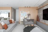 Grey sofa with rust cushions, a painting and a stone TV wall, Apartment Elache by Caroline Andrusko Arquitetos