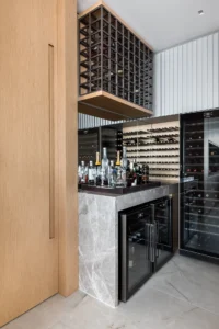 Bar with a stone counter, wine fridges and a bottle rack, Apartment Elache by Caroline Andrusko Arquitetos