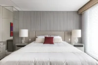 Primary bedroom with a white bed and a slatted grey wall, Apartment Elache by Caroline Andrusko Arquitetos