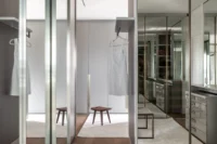 Walk-in closet behind glass doors with hanging rails, Apartment Elache by Caroline Andrusko Arquitetos