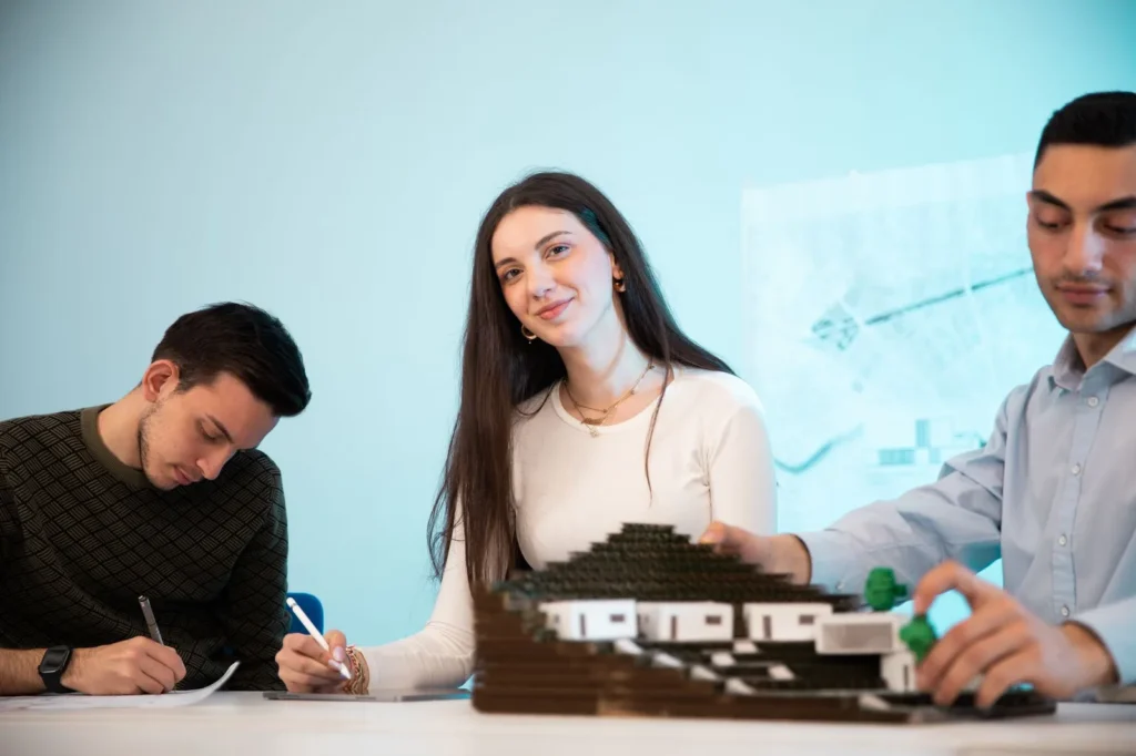 Three architecture students working around a building model and sketching at a table