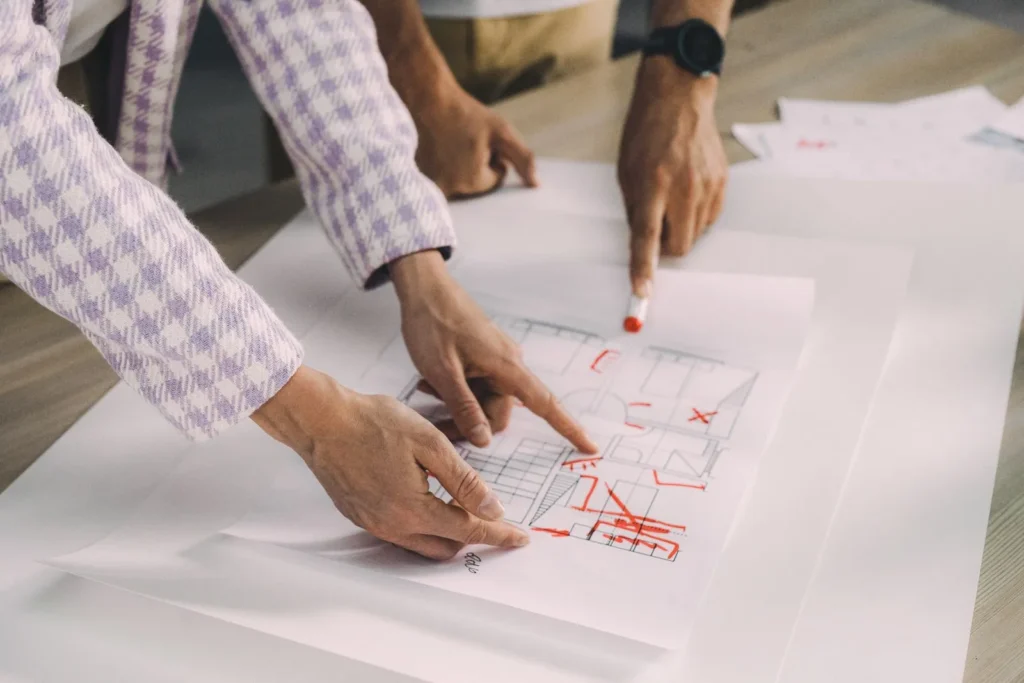 Two people marking up a floor plan in red pen during a design review, a checkpoint in the architectural design process