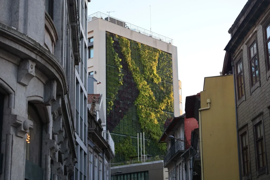 Vertical garden covering the side of a building between older stone facades on a narrow city street