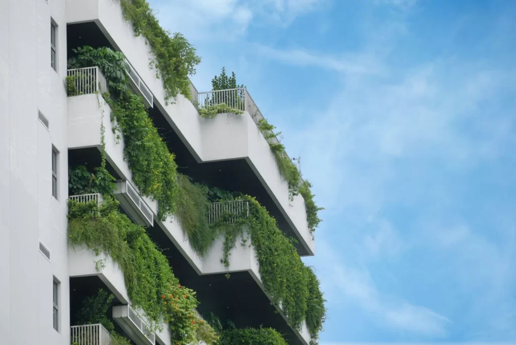 White apartment balconies overflowing with planted greenery against a blue sky