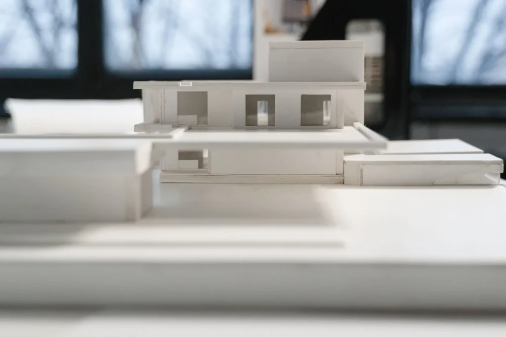 White study model of a low building on a desk, used to test massing before details are fixed