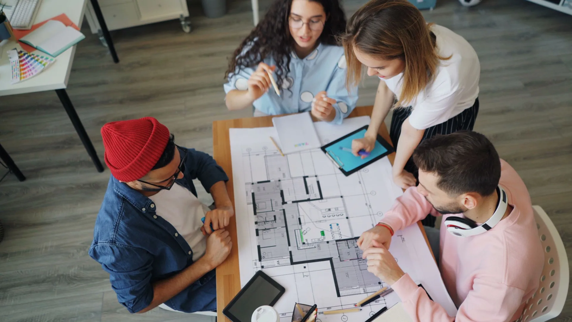 Architecture students reviewing a printed floor plan around a table with tablets and pencils