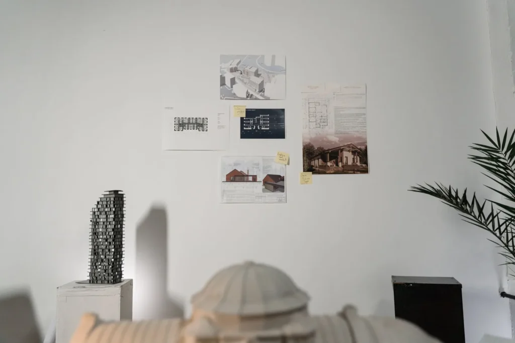 Presentation sheets with plans and images pinned to a white studio wall above a model
