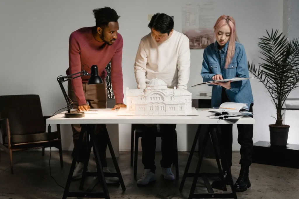 Three designers working around a white architectural model at a studio table