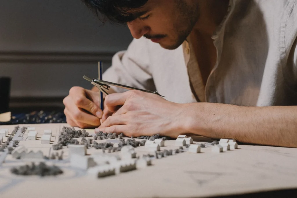 Young architect building a detailed site model with a compass at a cluttered studio desk
