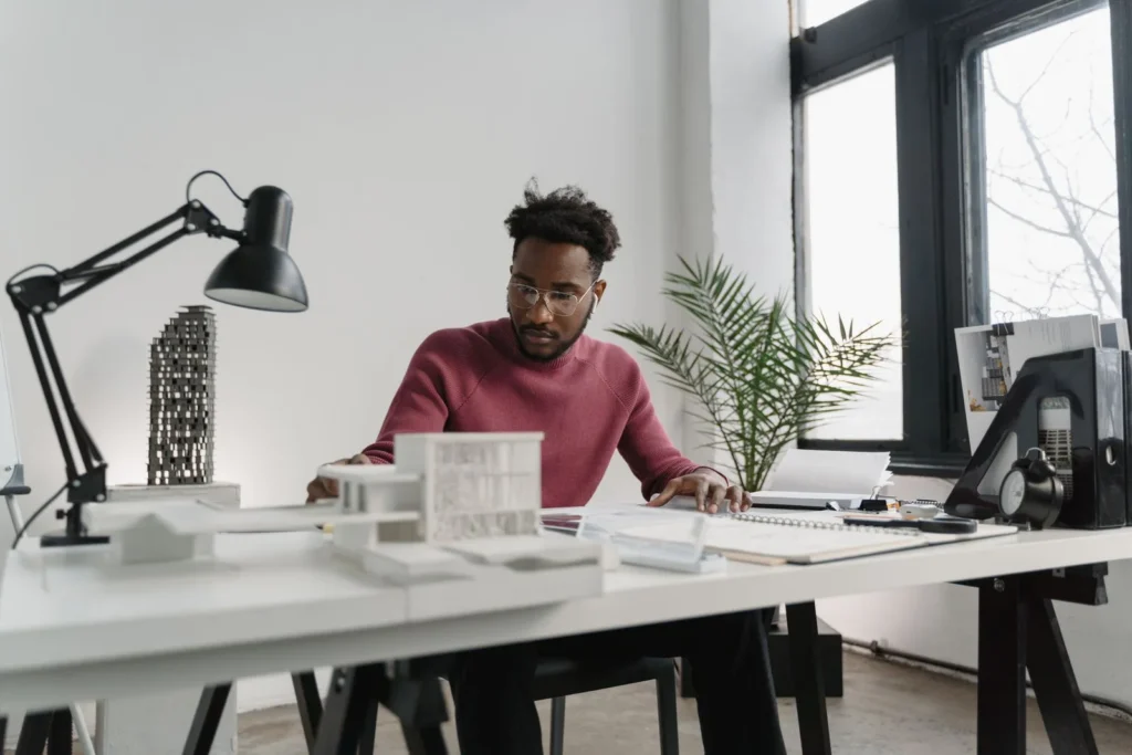 Architect working at a white desk with study models, a desk lamp and plans