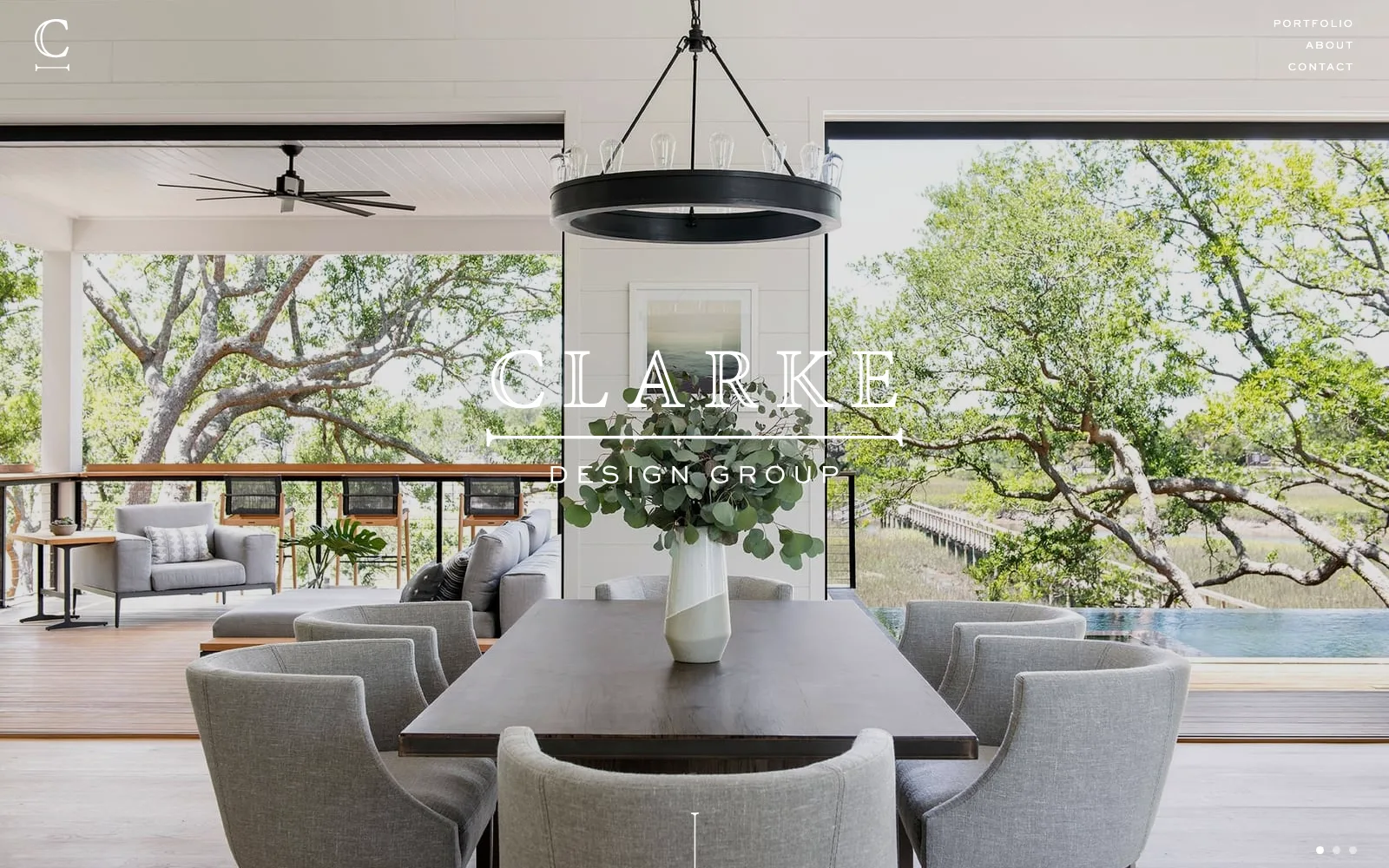 Clarke Design Group homepage showing a dining room with a black ring chandelier opening onto oak trees