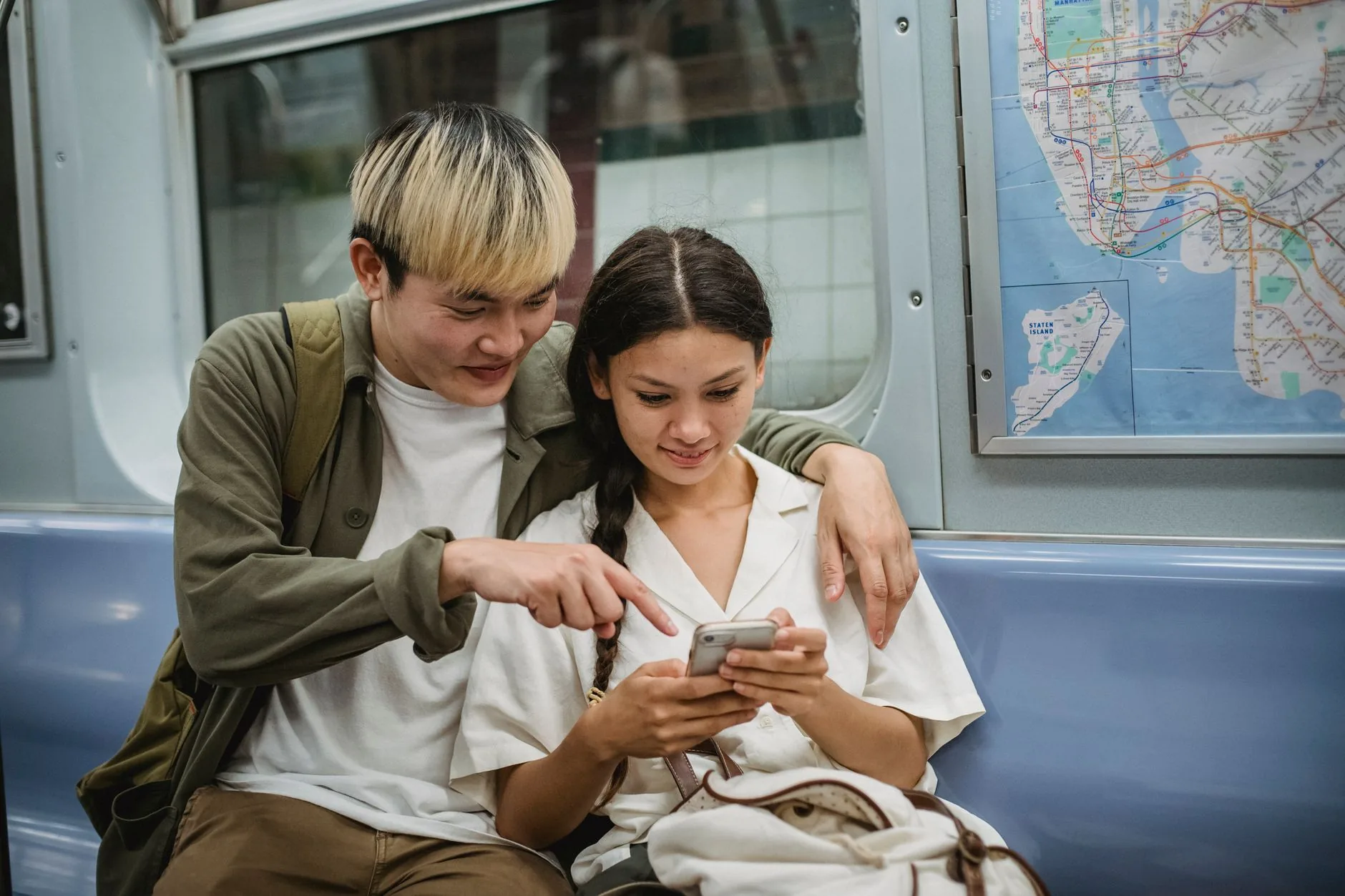 Two commuters on a subway train looking at a smartphone screen together beside a transit map