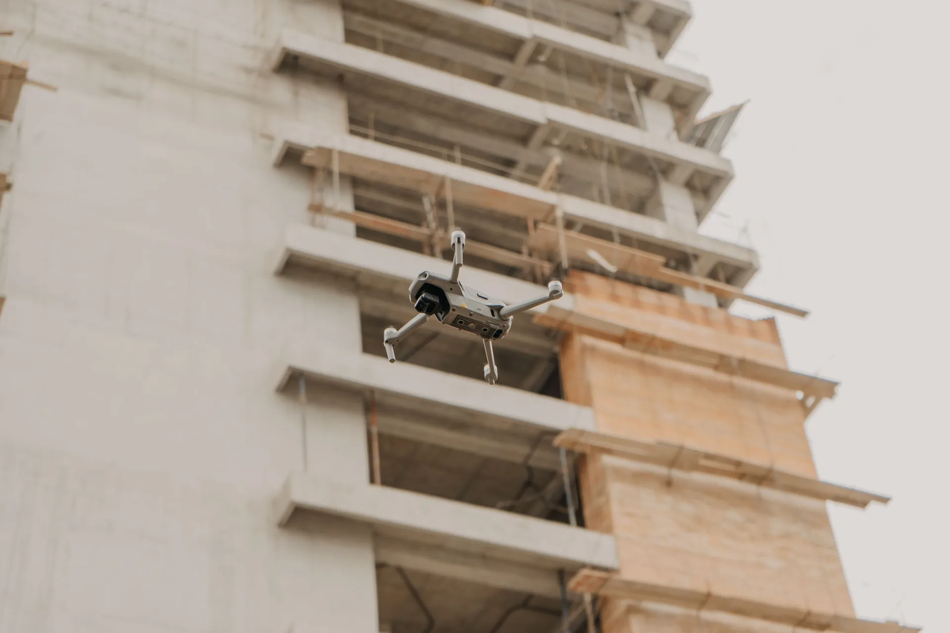 Compact folding drone hovering beside the concrete floor slabs of a building under construction