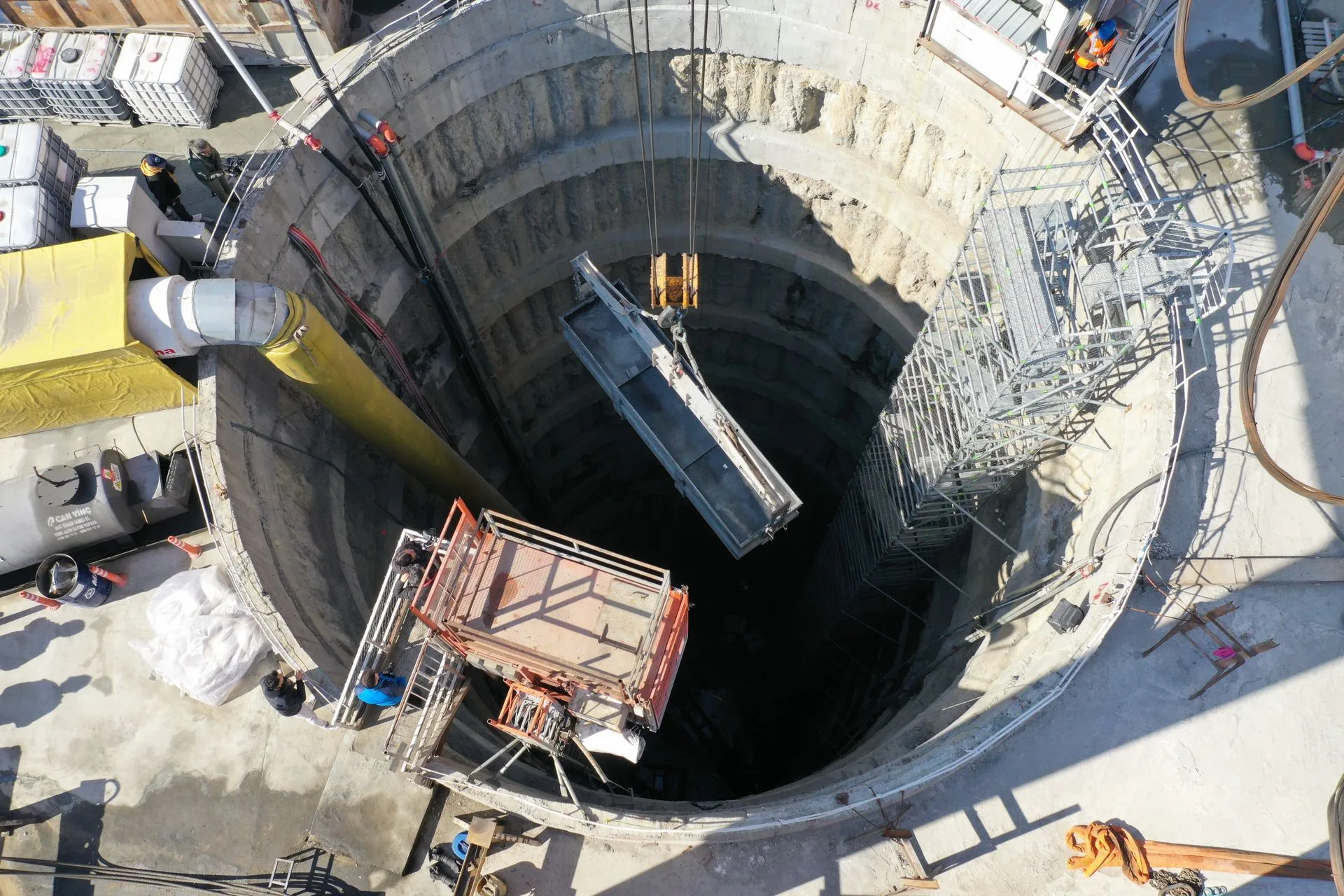 Aerial view of a deep circular shaft under construction with a lifting cage and scaffolding at the rim
