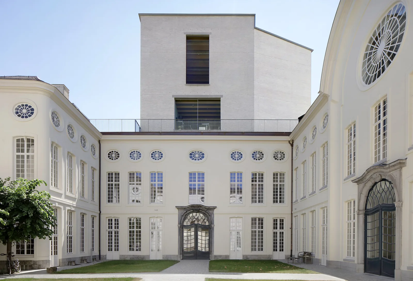 Renovated courtyard framed by a classical facade and a plain white extension under a blue sky