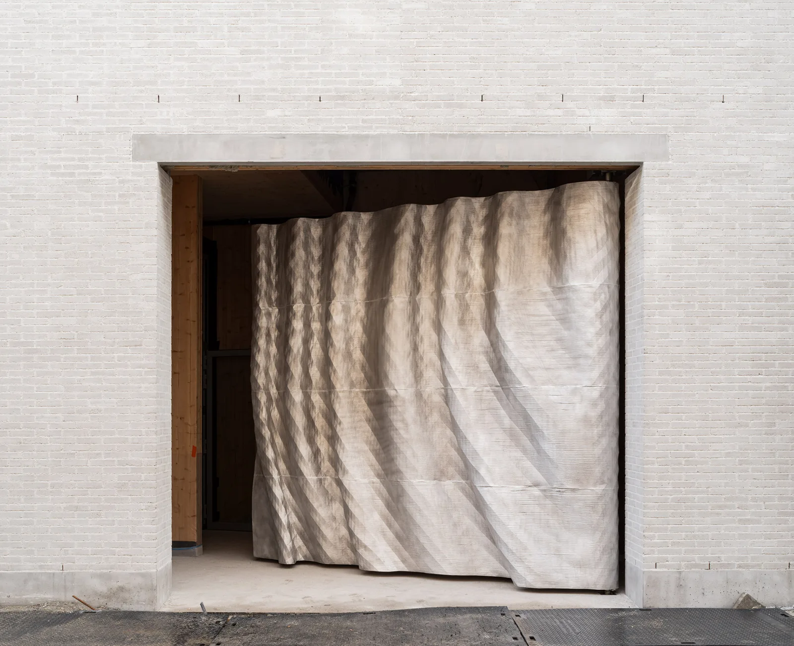 White brick wall with a deep rectangular opening and a rippled metal door