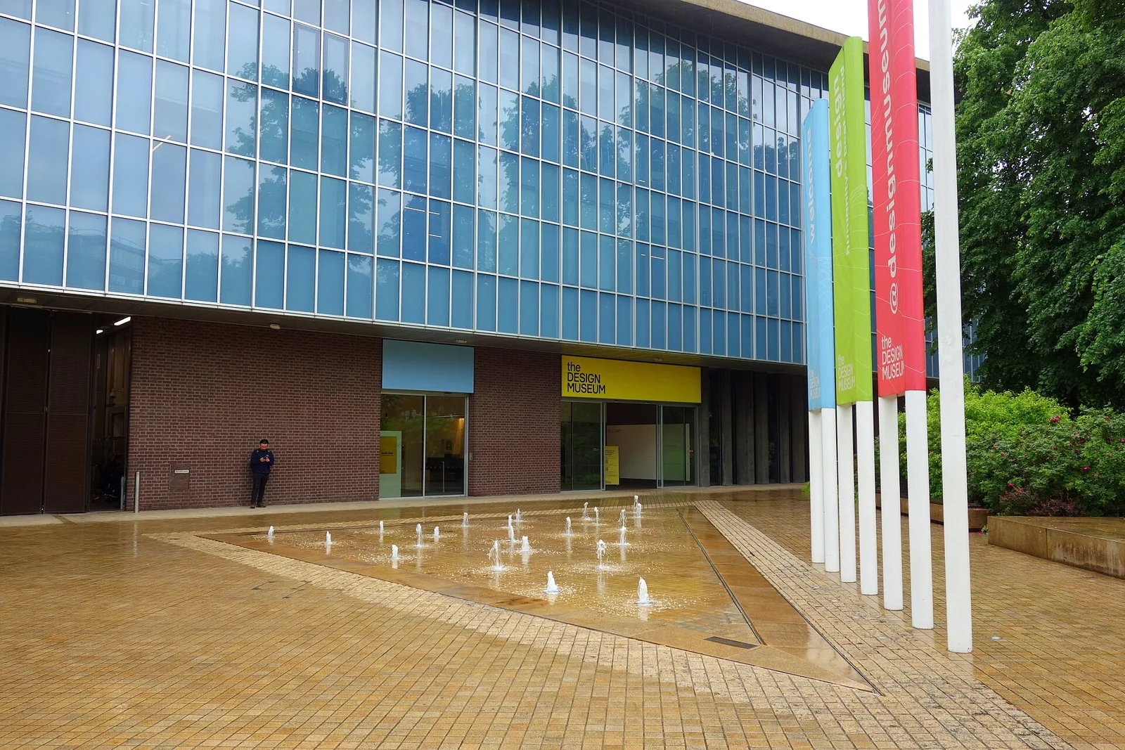 Glass and brick facade of the Design Museum in Kensington with banners and a forecourt water feature