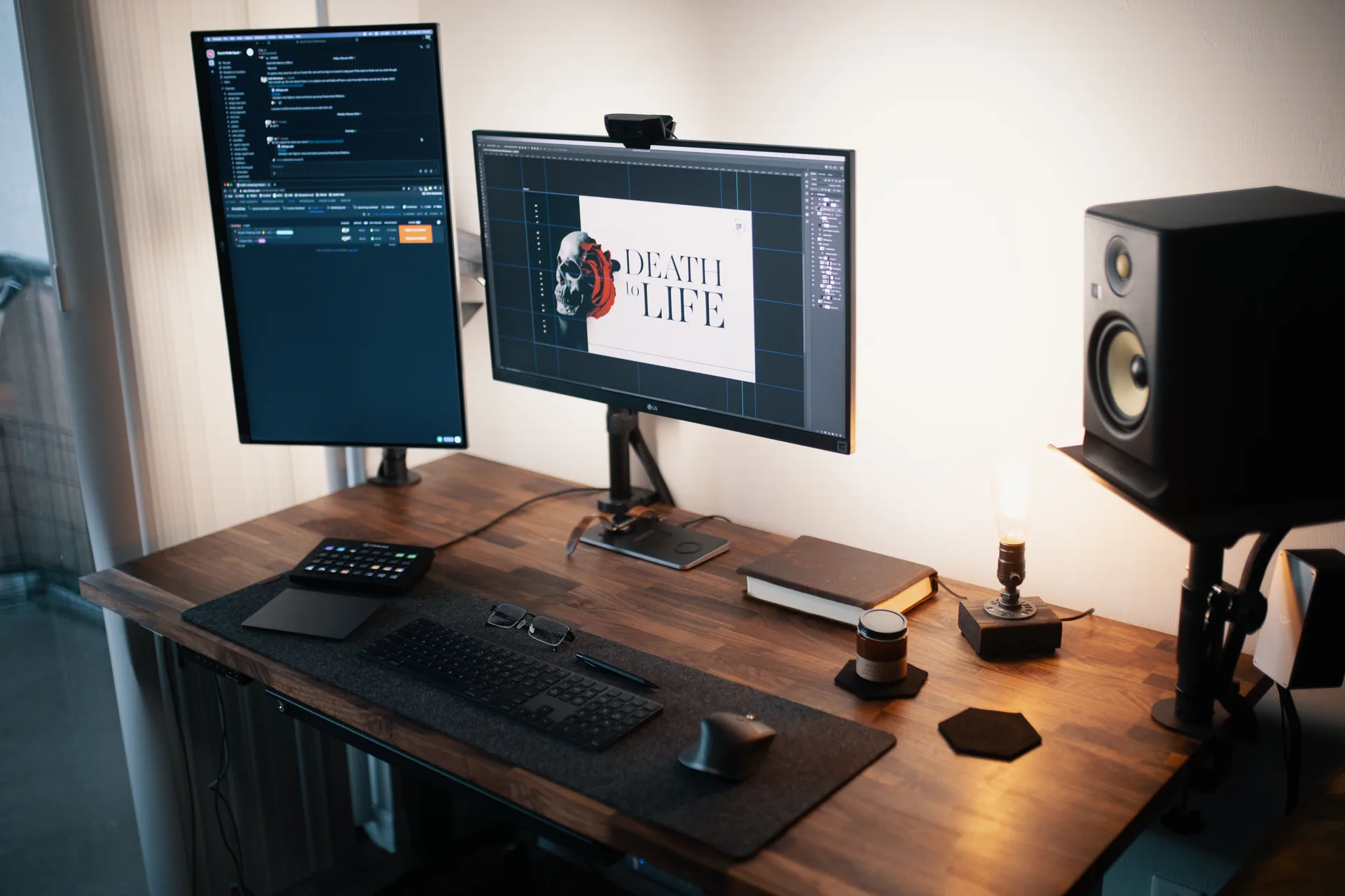 Desk with one monitor turned to portrait on an arm beside a landscape monitor, keyboard and studio speakers