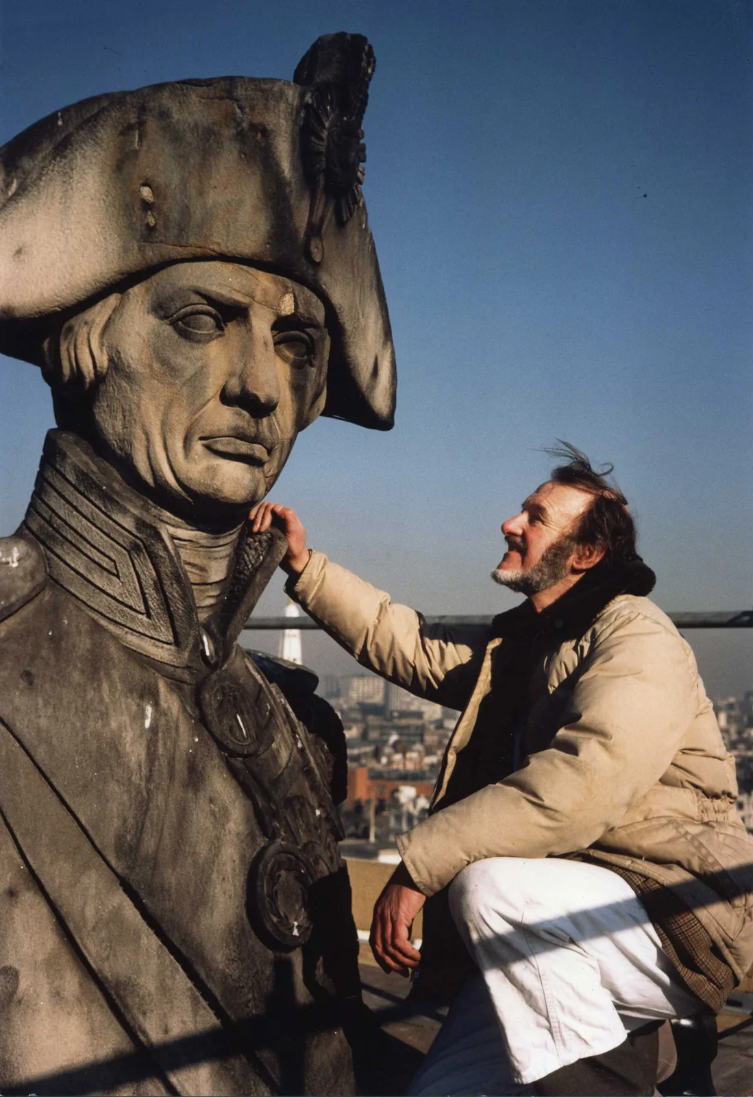 Donald Insall crouching beside the stone statue of Admiral Nelson at the top of Nelson's Column in London