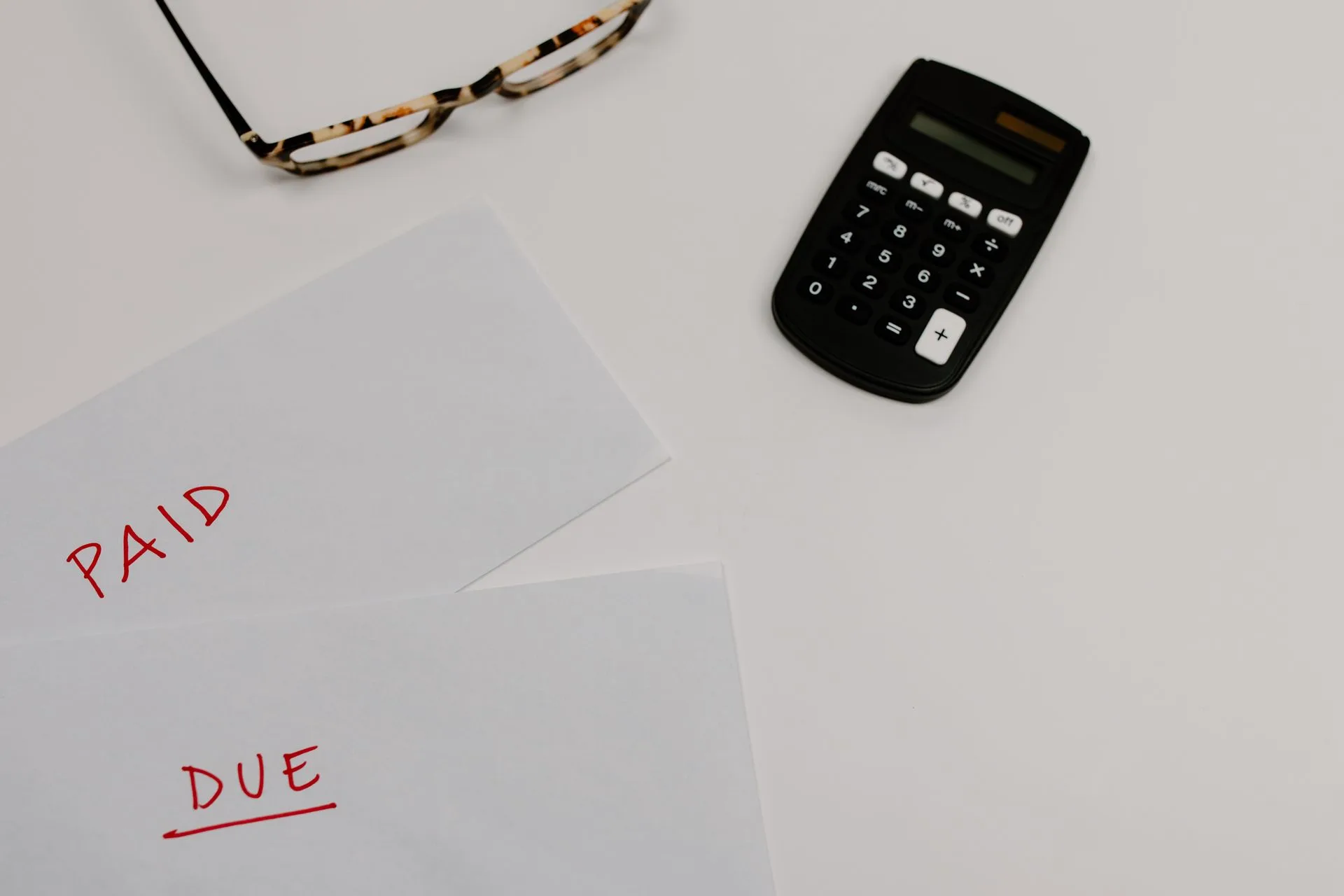 Bills stamped paid and due beside a calculator and glasses on a white desk