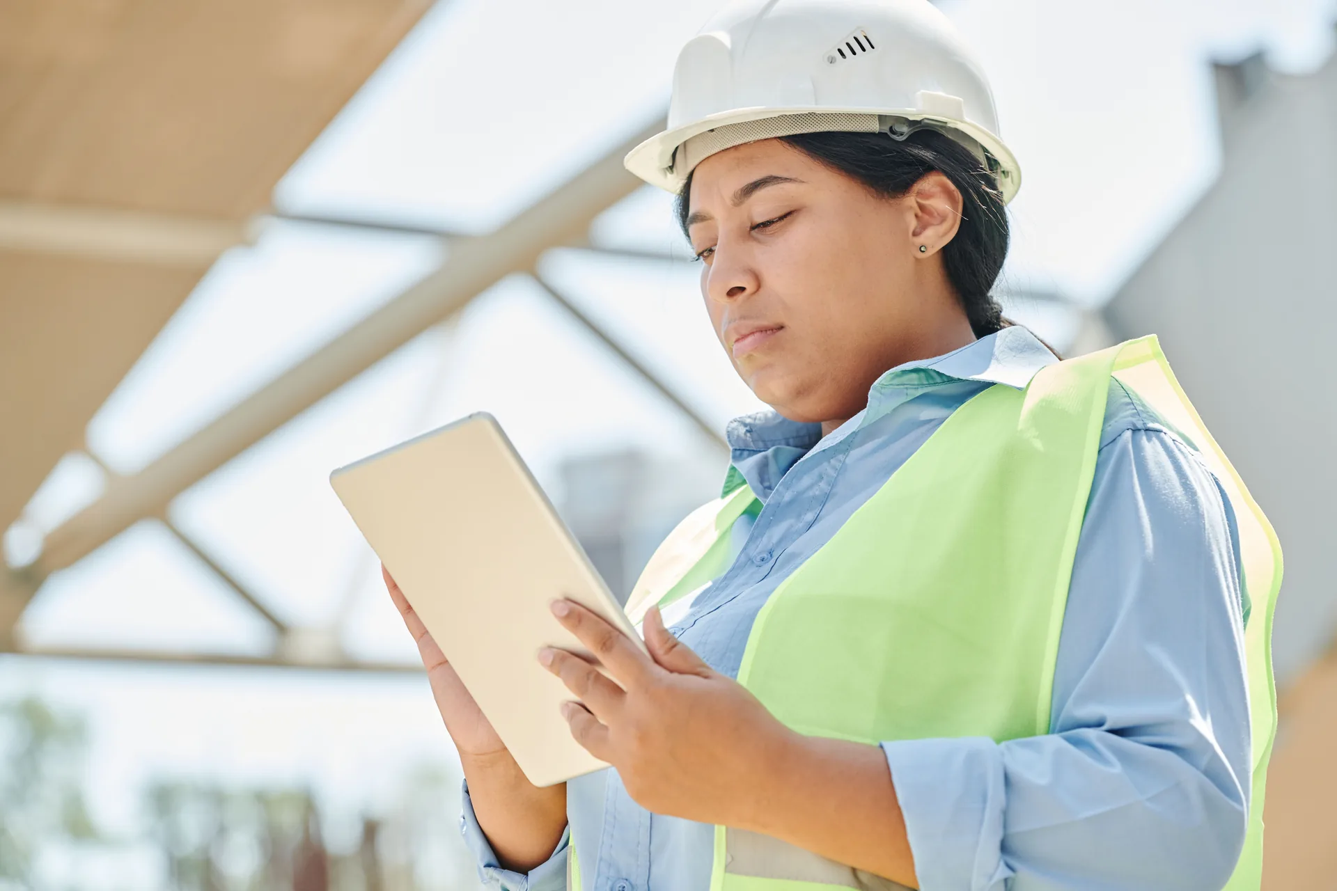 Engineer in a hard hat and high-visibility vest checking an estimate on a tablet at a construction site
