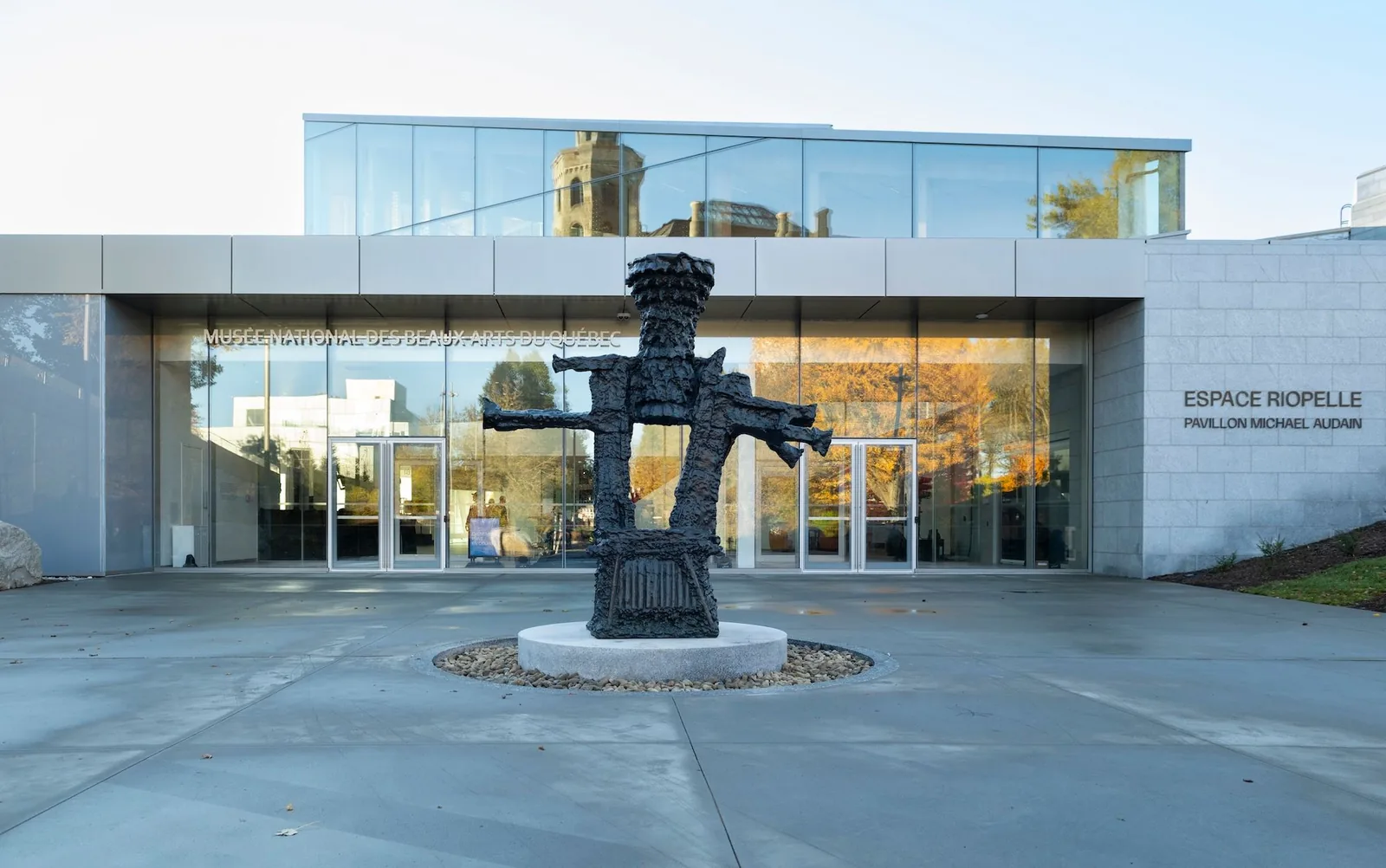 Glazed entrance of the Espace Riopelle with stone-clad walls and a dark bronze Riopelle sculpture on the front plaza