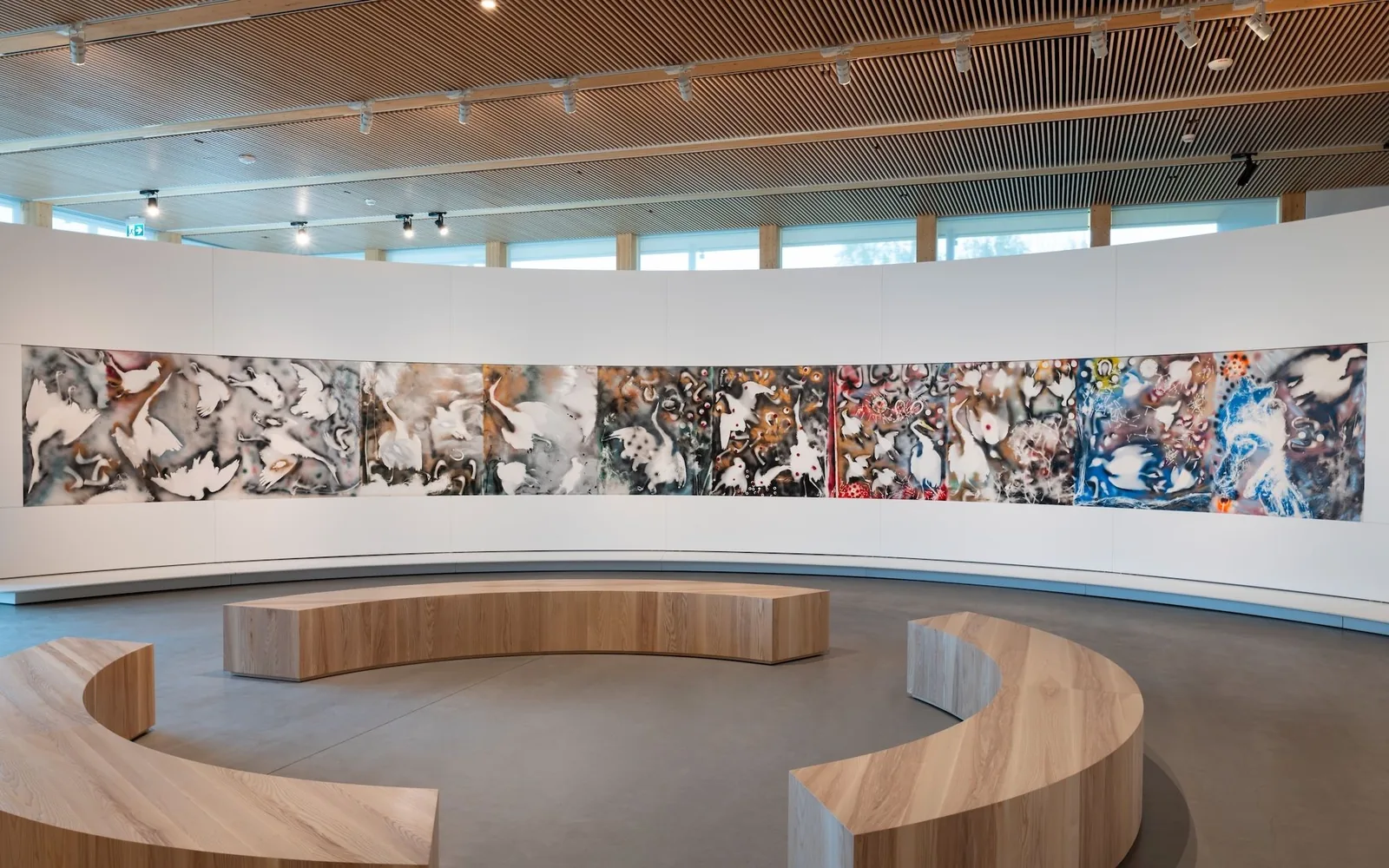 Curved gallery under a timber slatted ceiling with a long painted triptych wrapping the wall and curved wooden benches